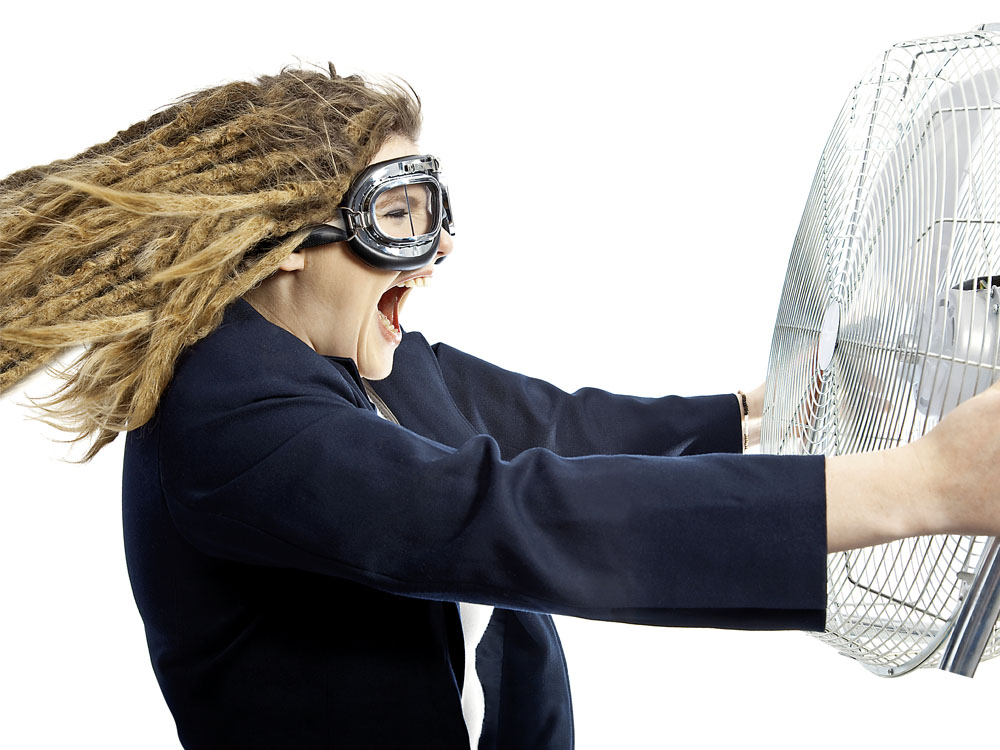 Frischer Wind - Frau mit einer alten Motorradbrille hält einen großen Lüfter hoch